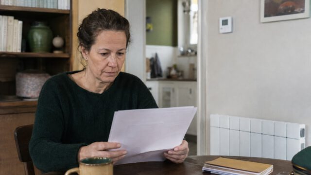 Une femme consulte des documents près d’un radiateur électrique dans son logement